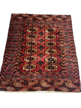Rectangular vintage Turkoman Tekke rug with red background and repeating octagonal motifs in yellow and brown, bordered by intricate geometric patterns in black and white.