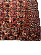 Close-up of a vintage Turkoman Tekke rug corner featuring geometric medallions in red, brown, and cream with a patterned border of white and black motifs.