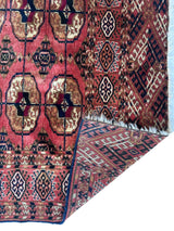 Close-up of a vintage Tribal Turkoman Tekke rug with geometric patterns in red, brown, black, and cream, showing detailed borders and a corner folded to reveal the reverse.