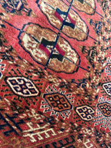 Close-up of a vintage Turkoman Tekke rug featuring red background with intricate geometric motifs in brown, cream, navy, and black, highlighting tribal pattern details.
