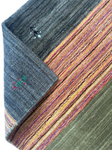 Hand-loomed Indo-Gabbeh runner rug folded to show dark gray woven reverse with simple floral motifs and striped front in orange, purple, and green hues.