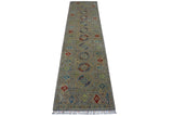 Long narrow hand-knotted Afghani Kazak wool rug with muted gray background, geometric medallions, multicolored accents, and fringes on one end.