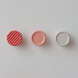 Three round coat hooks on a white wall, from left: red with diagonal ridges, smooth muted pink, and white speckled with small colorful dots.