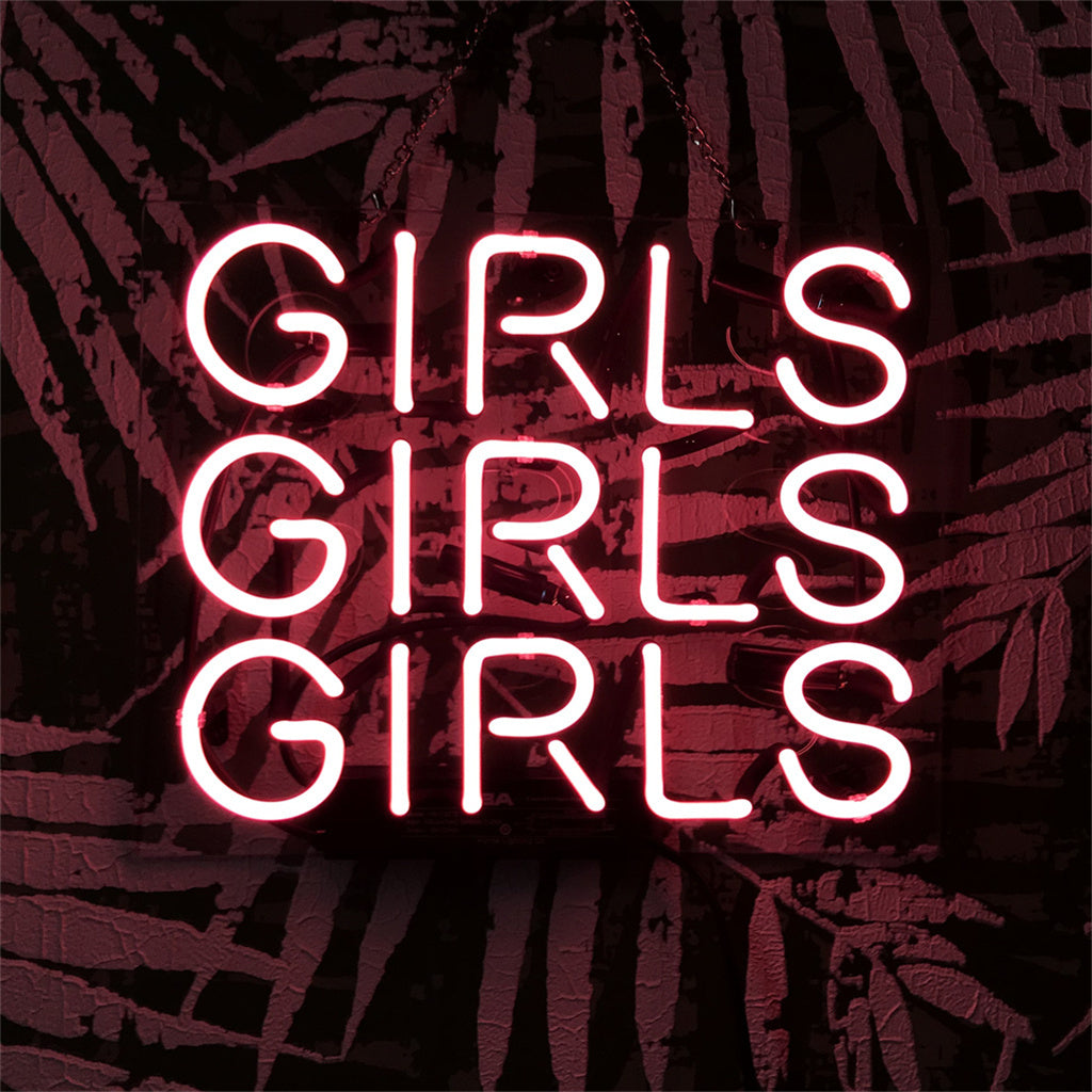 Pink neon sign repeating the word GIRLS three times in stacked lines against a dark wall with a leafy pattern background.