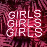 Pink neon sign displaying the repeated word 'GIRLS' three times in uppercase, mounted on a patterned wall with leaf designs in shadows.