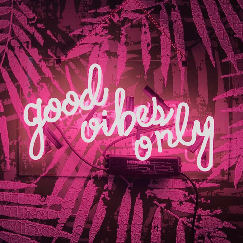 Pink neon sign reading 'good vibes only' mounted on a wall with a textured, abstract purple pattern casting shadows around it.