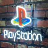 Neon light sign featuring the multicolored PlayStation logo above glowing white 'PlayStation' text, mounted on a dark metal frame against a brick wall.