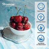 White bowl filled with fresh red cherries sitting on a clear, glossy epoxy coaster with irregular edges against a textured blue background.