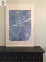 White-framed blue and white print of a locust tree cross-section with visible tree rings and cracks, displayed on a dark wooden dresser against a light wall.