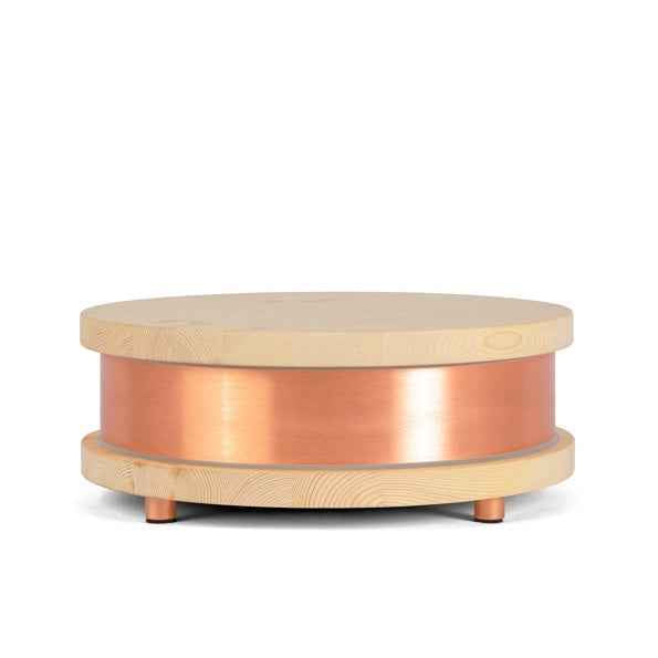 Round Qi-Home Cell with light wood top and base encasing a smooth copper cylindrical middle section, standing on small copper legs.