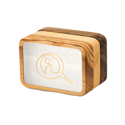 Three Qi-Me devices in Olive, Pine, and Walnut wood finishes displayed side by side on a white surface