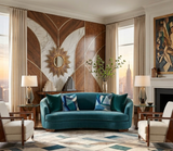Curved teal velvet sofa with blue geometric patterned pillows between two white armchairs in an art deco living room with wood and marble wall panels and brass sunburst mirror