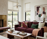 Living room with a deep rose-colored sofa adorned with patterned and solid pillows, a wooden coffee table with books and sculpture, and abstract art on the wall
