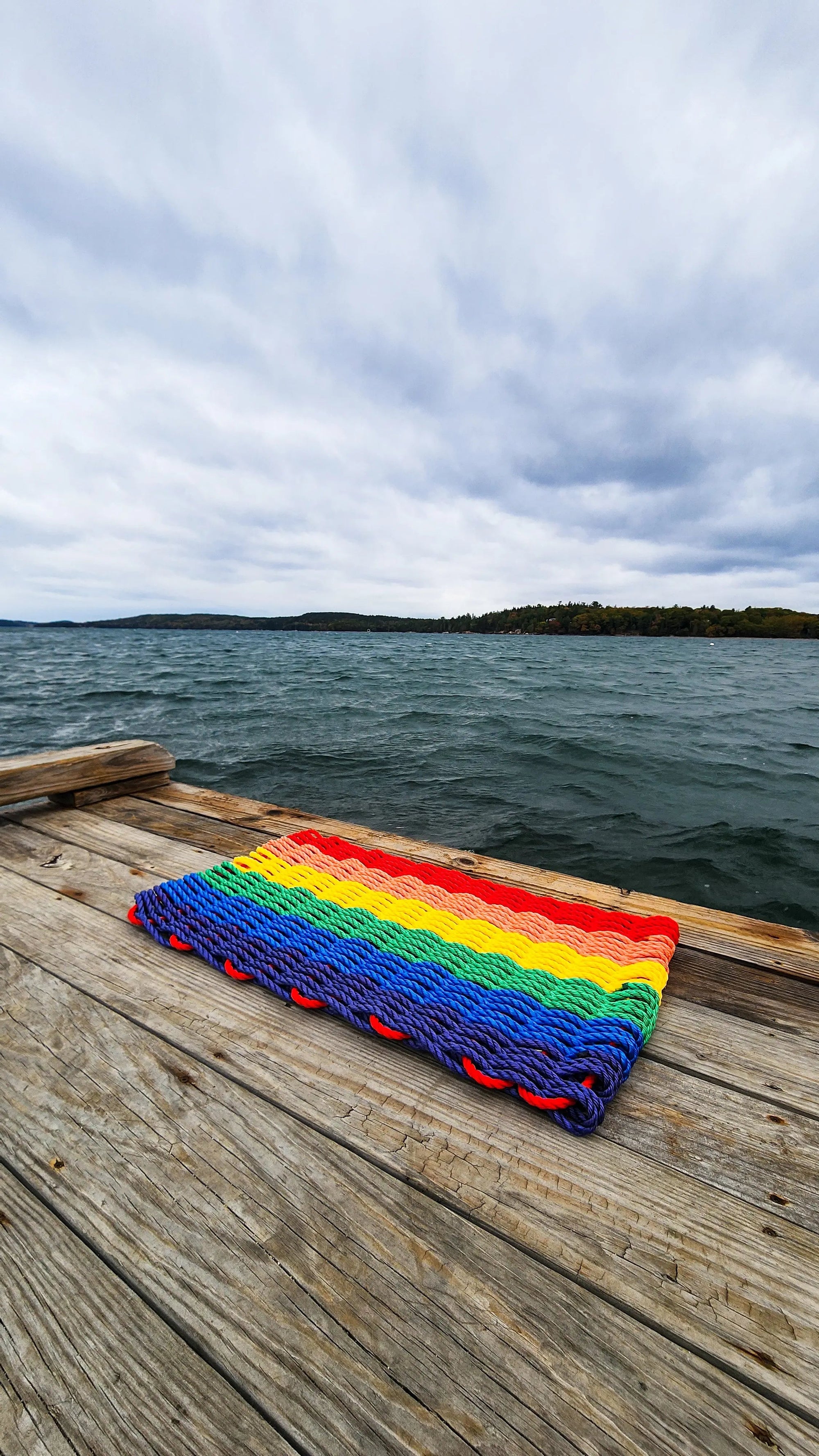Colorful handmade rainbow rope welcome mat made from lobster rope, displayed on a wooden floor