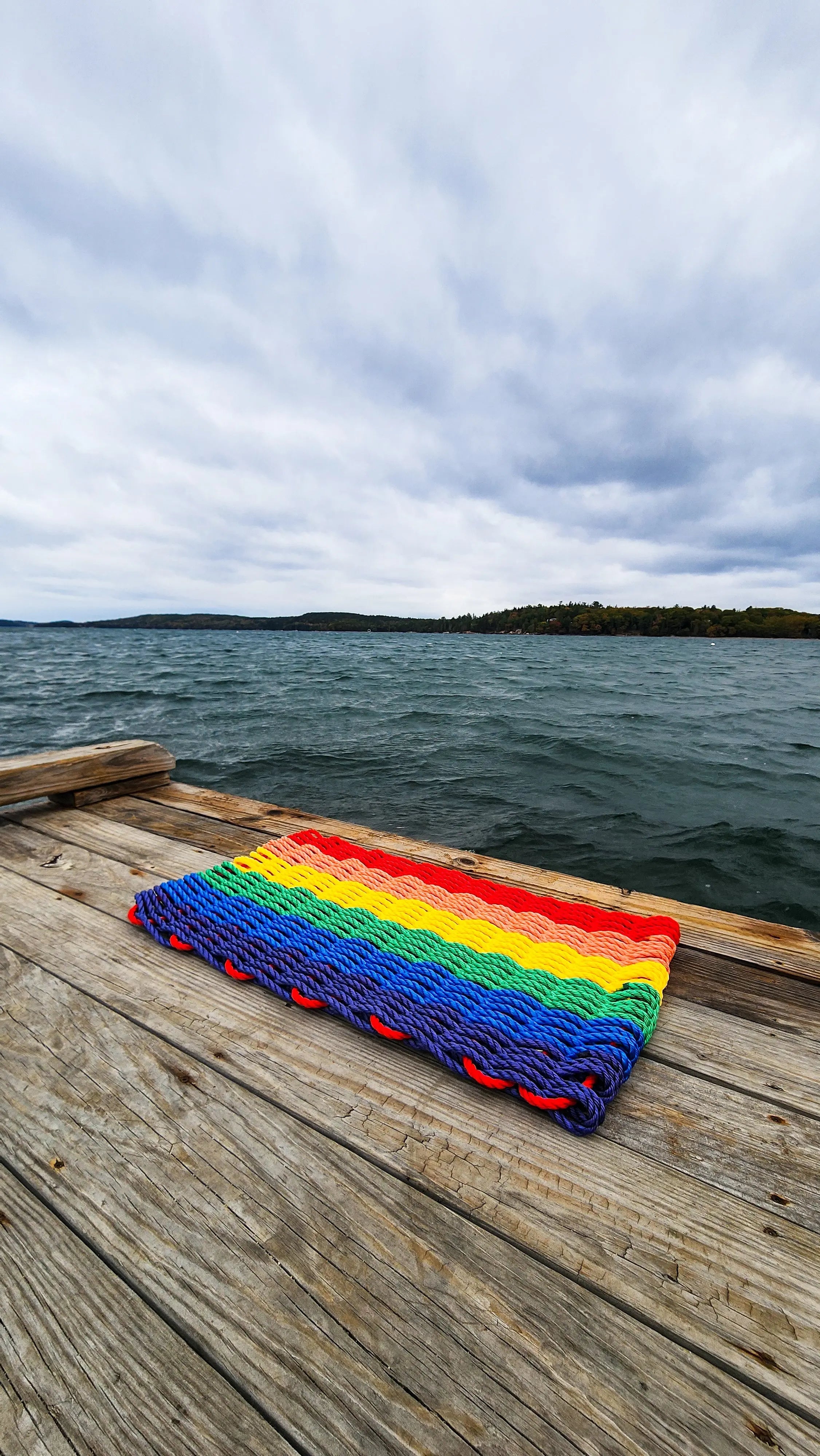 Colorful handmade rainbow rope welcome mat made from lobster rope, displayed on a wooden floor