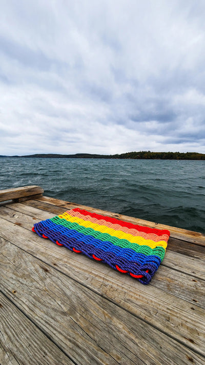 Colorful handmade rainbow rope welcome mat made from lobster rope, displayed on a wooden floor