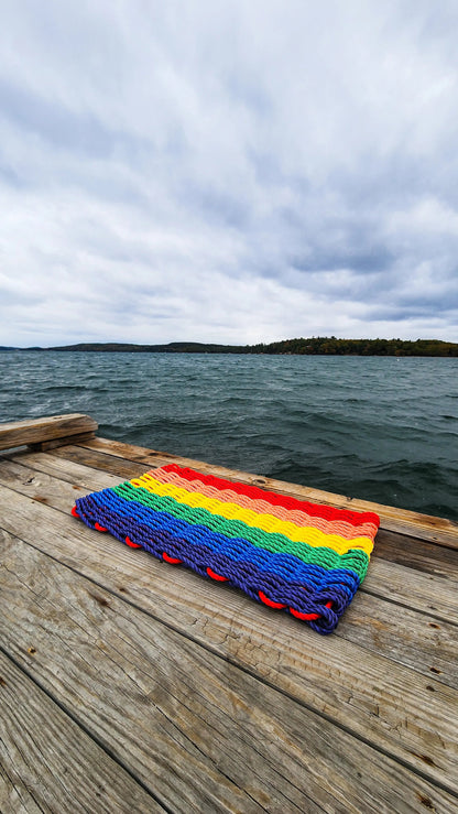 Colorful handmade rainbow rope welcome mat made from lobster rope, displayed on a wooden floor