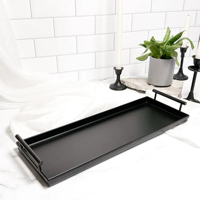 Gold metal rectangle tray on a white surface with decorative plants and candles