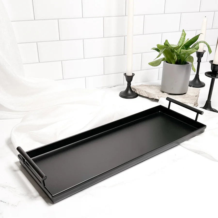 Black tray on a white surface with decorative items including candles and a plant.