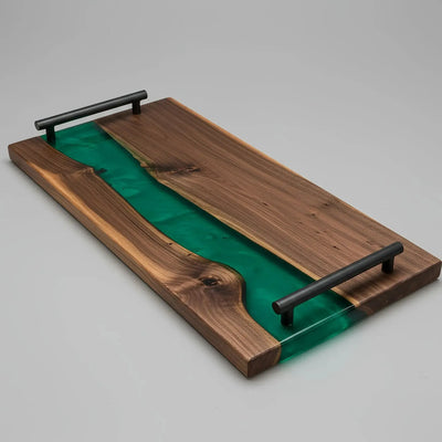 Handcrafted charcuterie board made from live edge black walnut wood with a glossy emerald green resin river running through the center, featuring matte black metal handles.