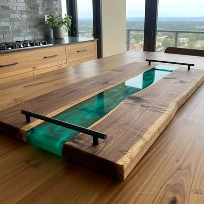 Handcrafted charcuterie board made from live edge black walnut wood with a glossy emerald green resin river running through the center, featuring matte black metal handles.