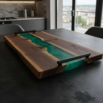 Handcrafted charcuterie board made from live edge black walnut wood with a glossy emerald green resin river running through the center, featuring matte black metal handles.