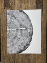 Black ink print of a pine tree cross-section showing detailed growth rings and a horizontal crack, on white paper placed on rustic wooden surface.