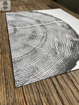 Close-up of a black and white print showing detailed tree rings on white paper, placed diagonally on textured rustic wood surface.