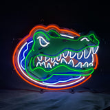 Neon sign of a stylized alligator head with green outline and white teeth inside an orange and blue oval background on a dark surface