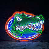 Neon sign depicting a green alligator head with white teeth inside an orange oval outline, detailed with blue and white neon accents on a black background.