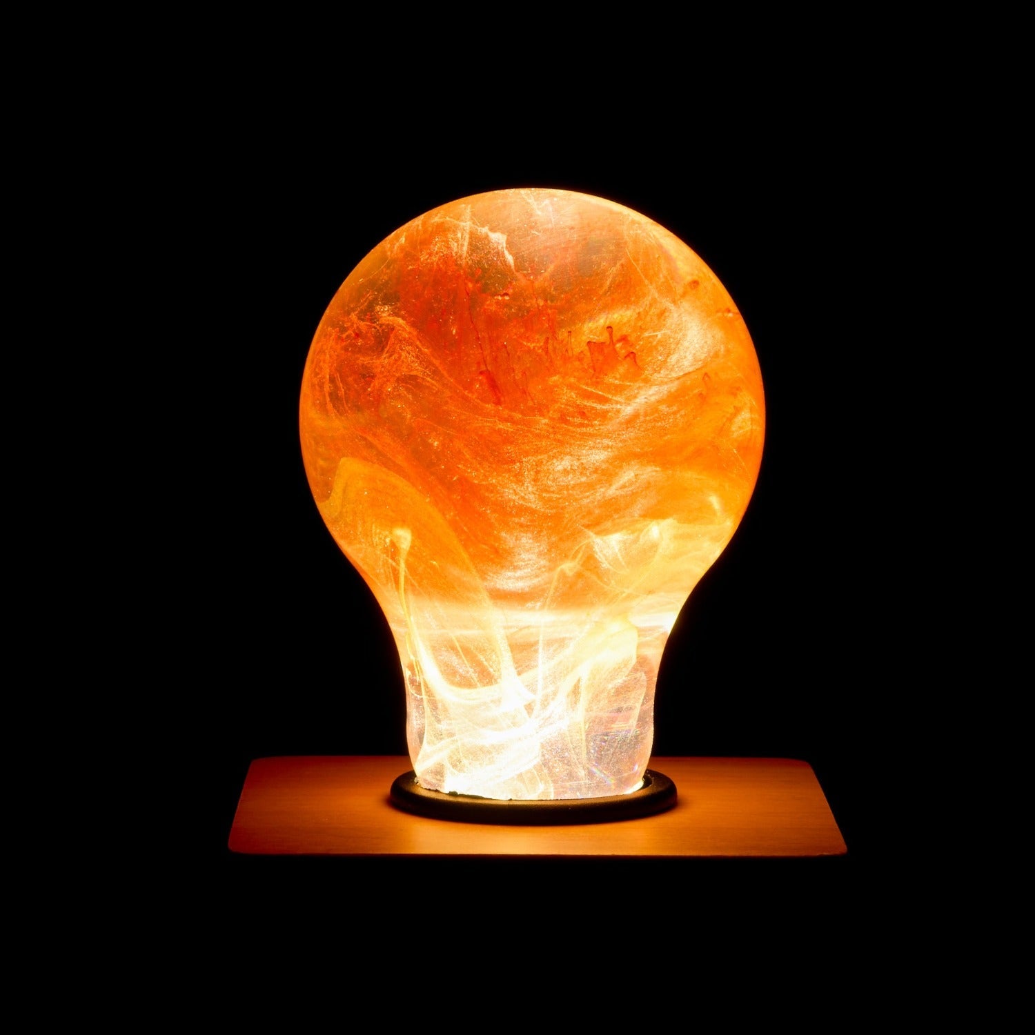Decorative resin lamp shaped like a light bulb with a warm glow on a black background