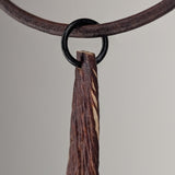 Thin pendant with textured dark brown and beige diagonal stripes hanging from a round black ring on a brown leather cord against a plain background.