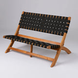 Wood-framed folding bench with wide black woven straps on seat and backrest, angled legs, and a minimalistic design, shown against a plain gray background.
