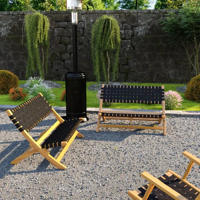 Two wooden benches with black woven straps, angled legs, and natural finish, set on gravel in a garden with trimmed bushes and tall hanging plants against a stone wall.