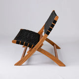 Side view of a low-profile wooden folding chair with a natural finish frame and black woven fabric straps on the seat and backrest
