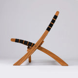 Side view of a wooden folding chair with curved legs and backrest wrapped in black fabric bands, shown against a plain light gray background.