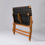 Rear view of a teak and black woven strap folding bench with wooden hinges, set against a plain gray background.