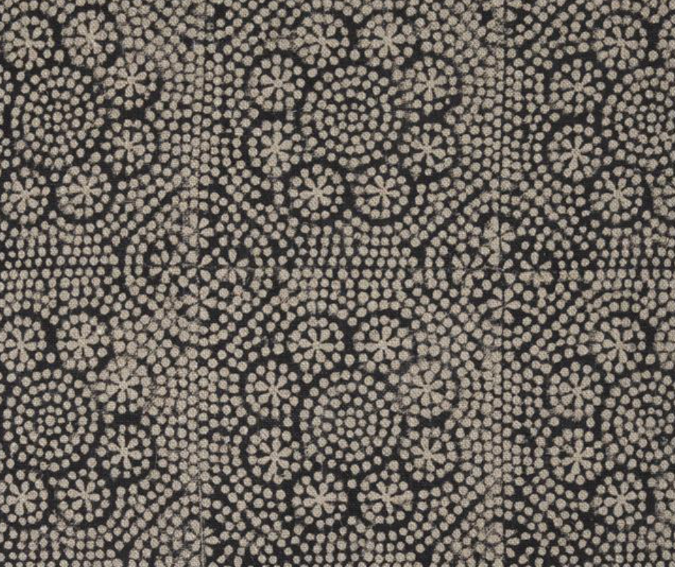 Close-up of a black fabric with a beige floral pattern made of small dots arranged in spirals and flower shapes.