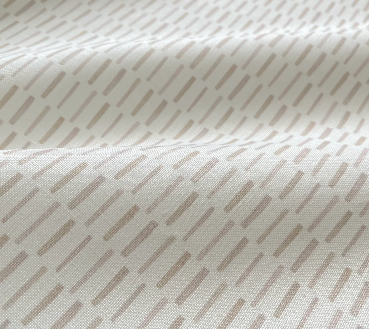 Close-up of off-white fabric with pale taupe elongated dash pattern, showing soft folds and subtle texture under natural light.