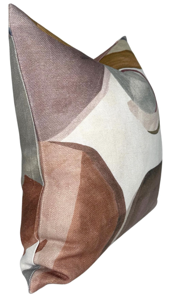 Square pillow with abstract geometric shapes in muted earth tones including brown, beige, and gray, shown from a side angle with visible seam details.