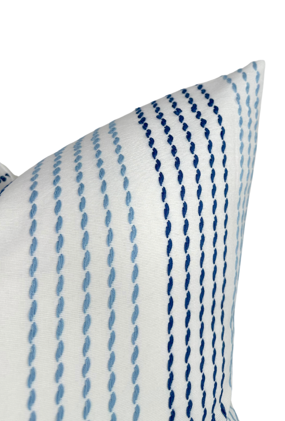Corner of white pillow cover featuring parallel rows of embroidered running stitches in varying shades of blue, from light to dark, on a smooth fabric.