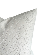 Close-up of a light oyster-colored pillow cover featuring subtle wavy embroidery creating a textured, flowing pattern on smooth fabric.