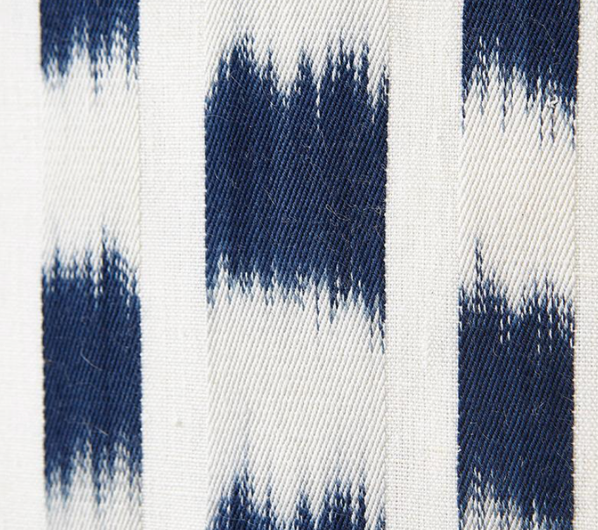 Close-up of indigo blue and white striped fabric with a blurred, ikat-inspired pattern on textured woven cotton.