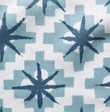 Blue starburst shapes with eight points centered on lighter blue cross patterns against a white background in a repeating textile design.