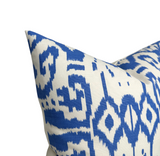 Close-up of a pillow with a white background featuring a bold royal blue ikat pattern of geometric and diamond shapes, showcasing textured fabric detail.