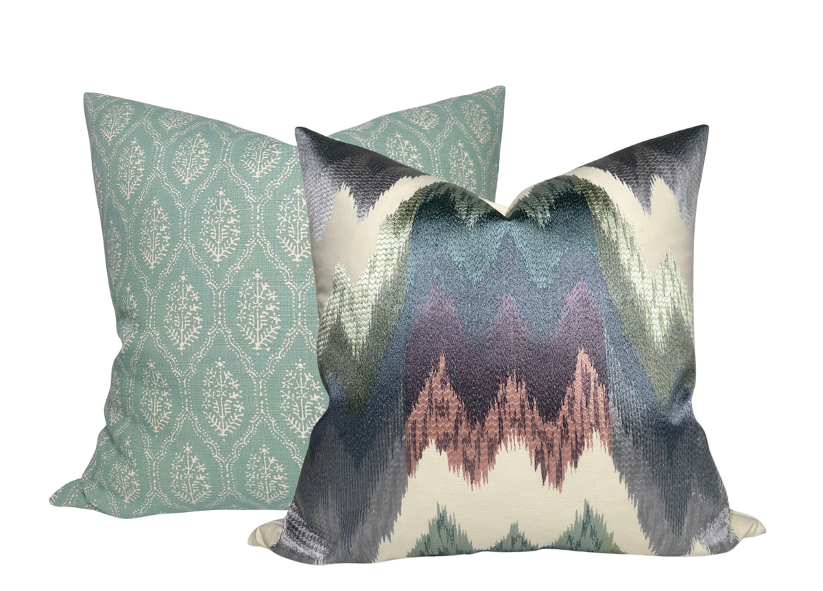 Two decorative pillows, one with a teal pattern of vertical oval leaf motifs and the other with an abstract zigzag gradient in shades of blue, gray, and mauve.