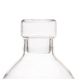 Transparent glass bottle stopper with a cylindrical top and a narrower neck designed to fit small bottles, shown against a white background.