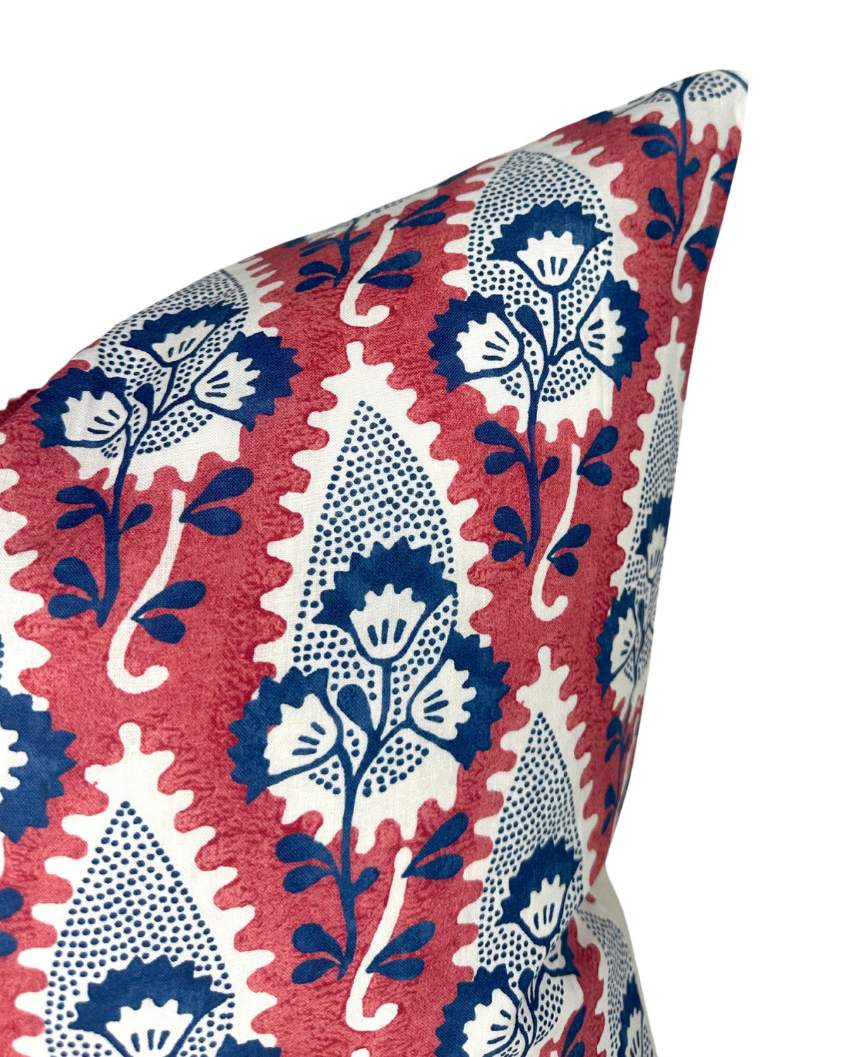 Corner of a pillow with a red background featuring a repeating pattern of stylized blue and white floral motifs within pointed oval shapes.