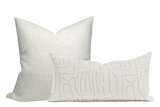 Two white pillow covers: one square with a subtle woven texture, one rectangular with an abstract stitched line pattern in light beige.