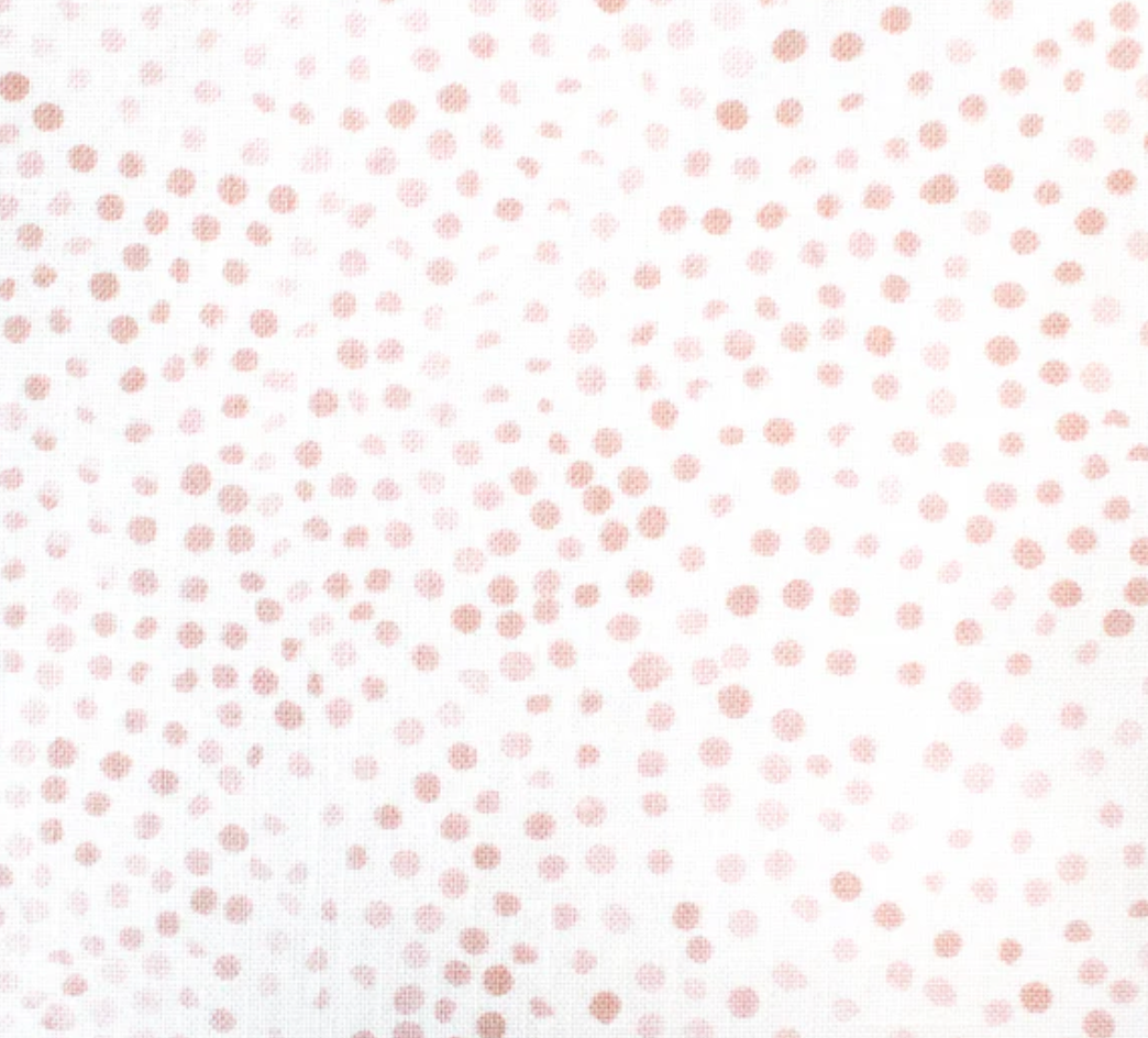 Fabric featuring a white background scattered with irregular blush pink dots varying in size and spacing, creating a delicate speckled pattern.